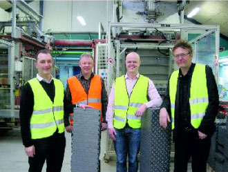 Der Geschäftsführer von MAGU Bausysteme steht mit den Partnern in Warnwesten in einer Produktionshalle in Dänemark und präsentieren verschiedene MAGU-Bauelemente.