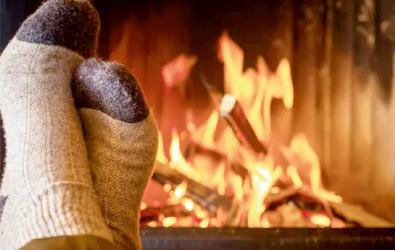 Gemütliche Atmosphäre mit warmen Wollsocken vor einem Kaminfeuer – Symbol für Behaglichkeit und Wärmeschutz.